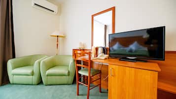 A hotel room with a green sofa, a wooden desk, a television, and a mirror.
