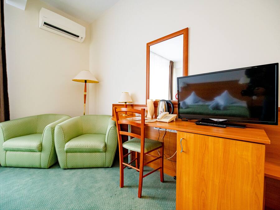 A hotel room with a green sofa, a wooden desk, a television, and a mirror.