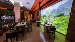 A restaurant with multiple tables and chairs, a large window with a view of mountains, and a sign reading "RIVULUS".