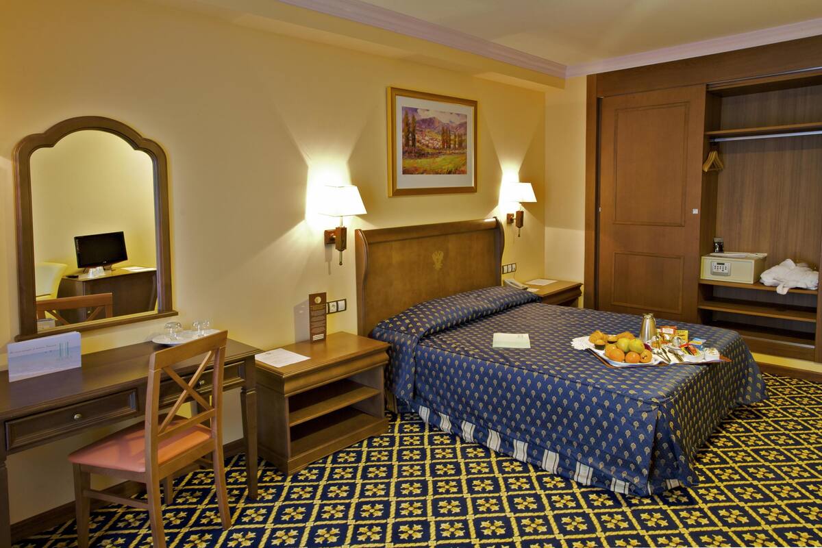 Een hotelkamer met een bed, bureau, stoel en een grote spiegel.