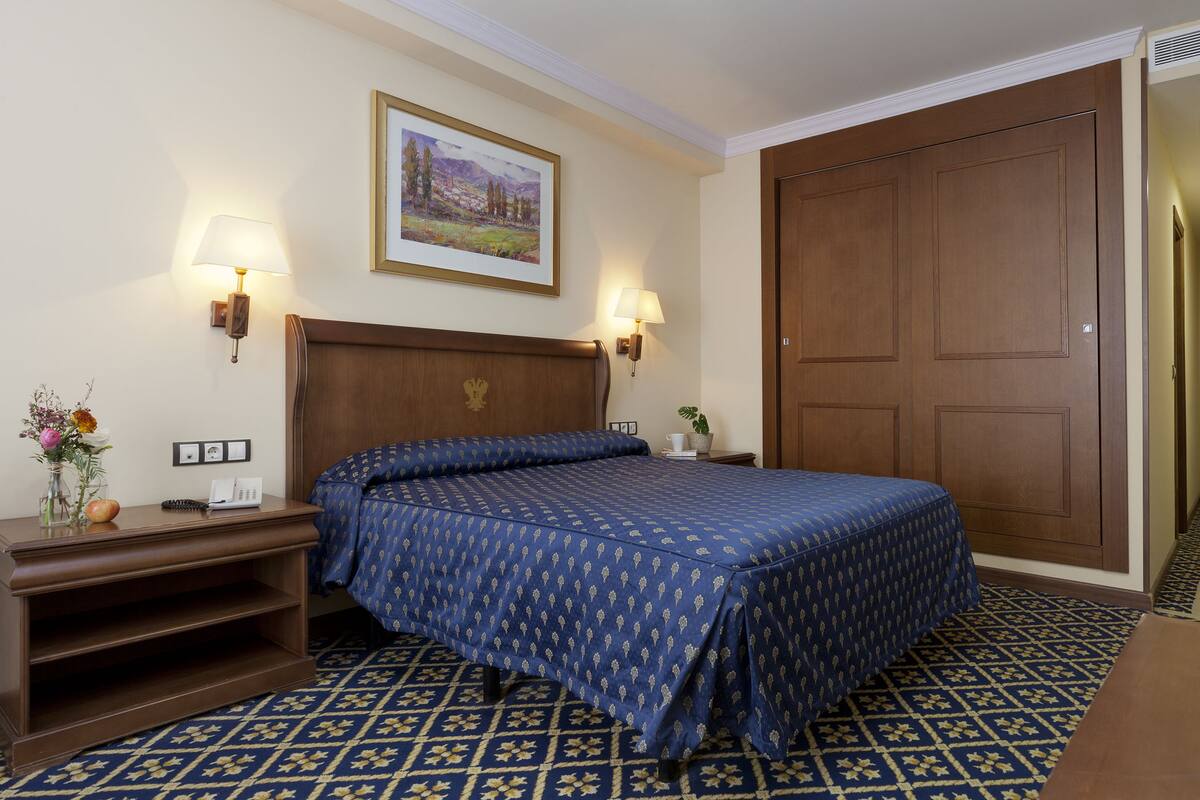 Een hotelkamer met een groot bed, een houten garderobe, een bureau met lamp en een lijst met afbeelding aan de muur.
