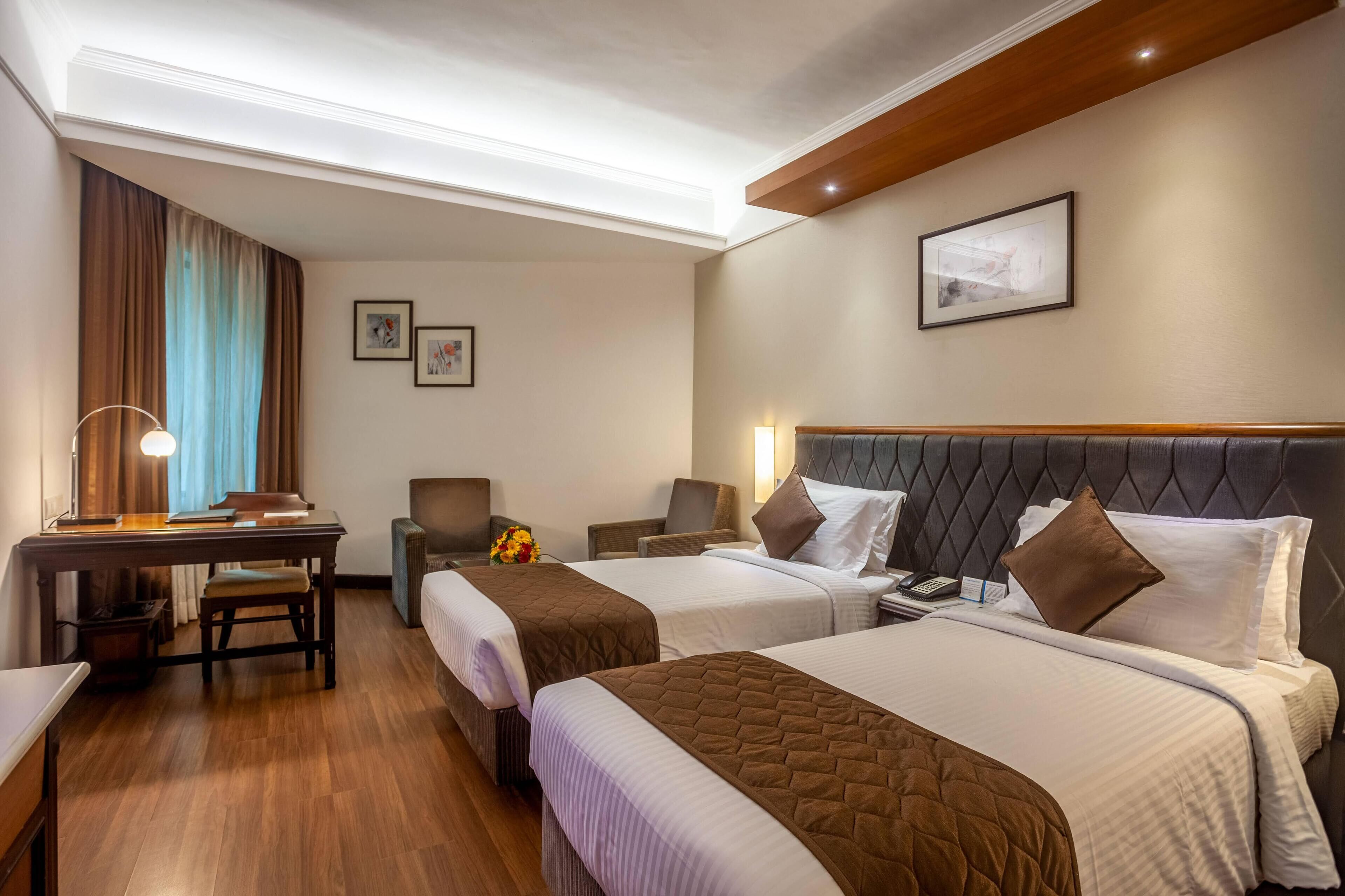 Habitación de hotel con dos camas, un escritorio, una silla y una mesita.