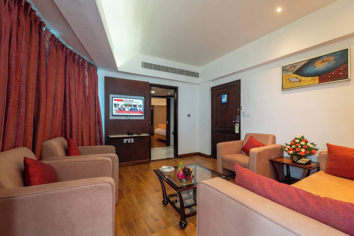 A hotel room with a sofa set, a small table with a vase of flowers, and a painting on the wall.