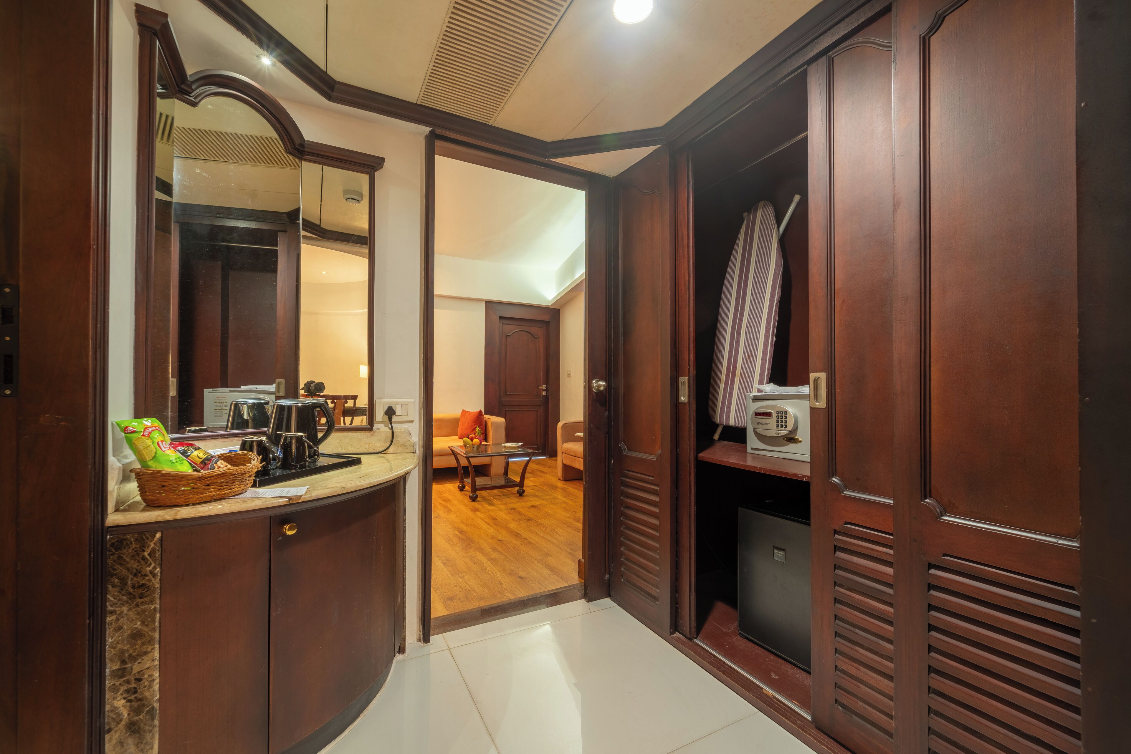 A hallway with a wooden wardrobe, a kitchen area with a coffee maker, and a living room with a sofa and a table.