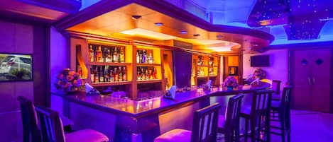 A bar area with a curved counter, multiple bar stools, and shelves stocked with bottles.