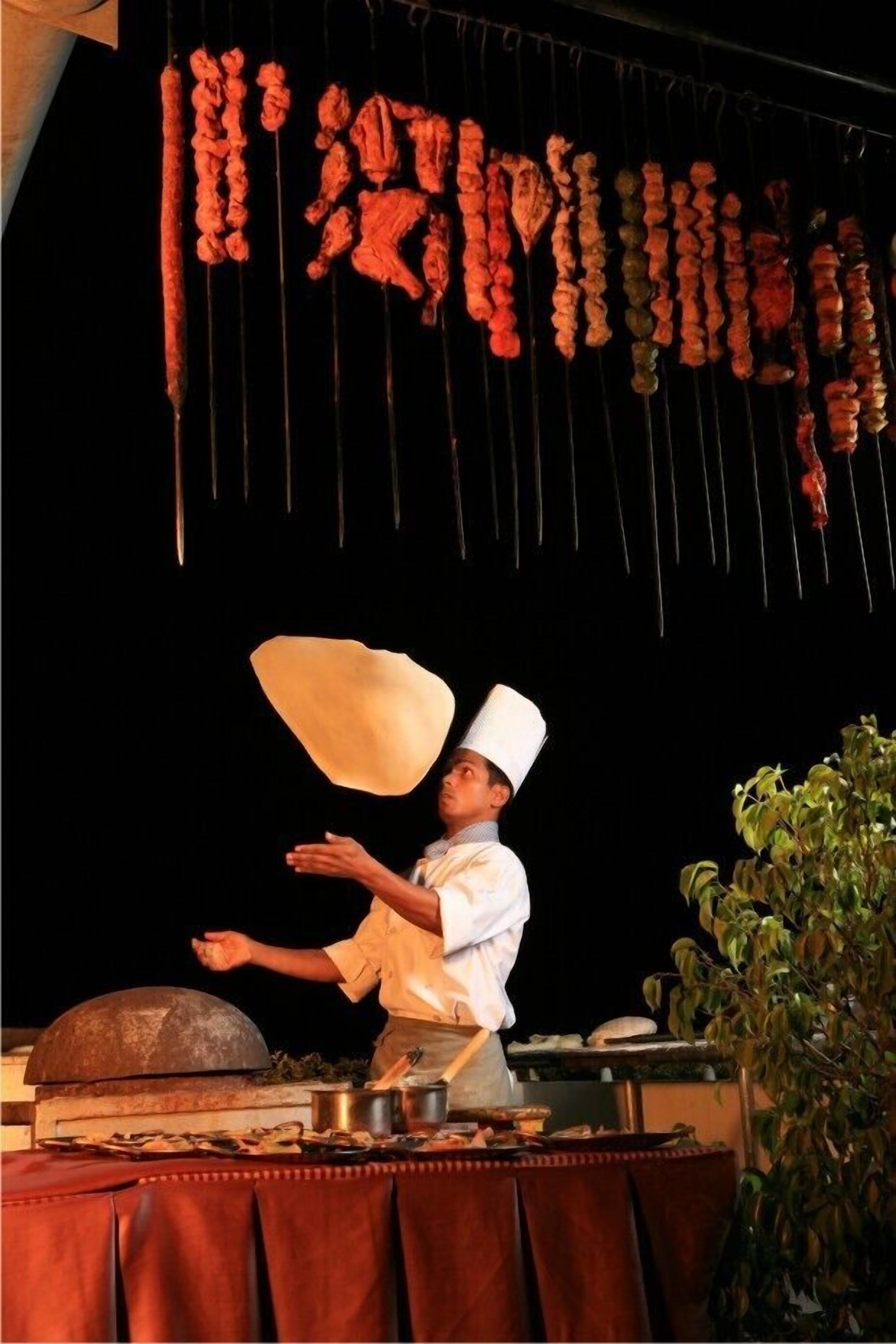 A chef performing a cooking demonstration with skewers hanging above a grill.