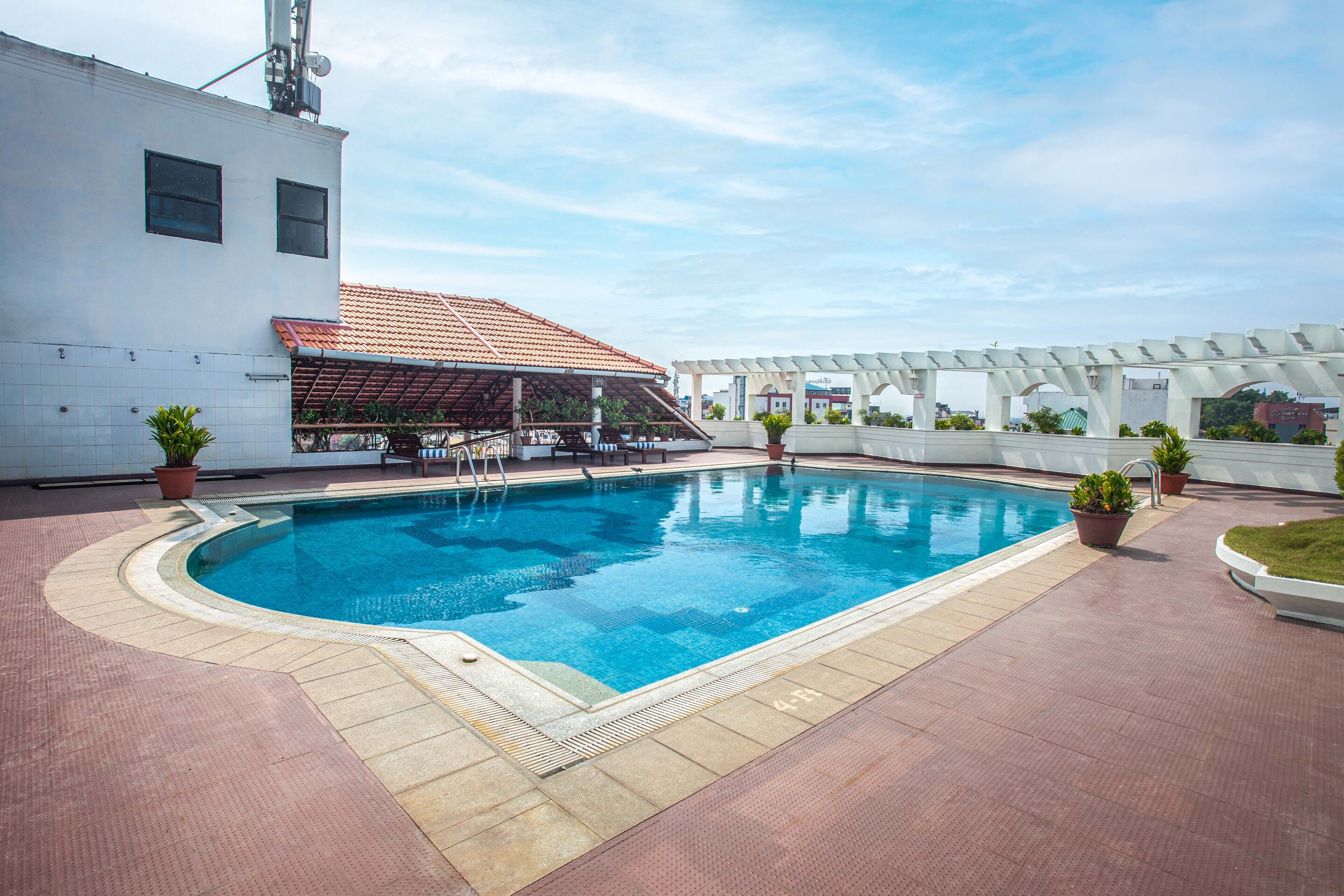 A rooftop swimming pool with a tiled deck, potted plants, and a covered seating area.