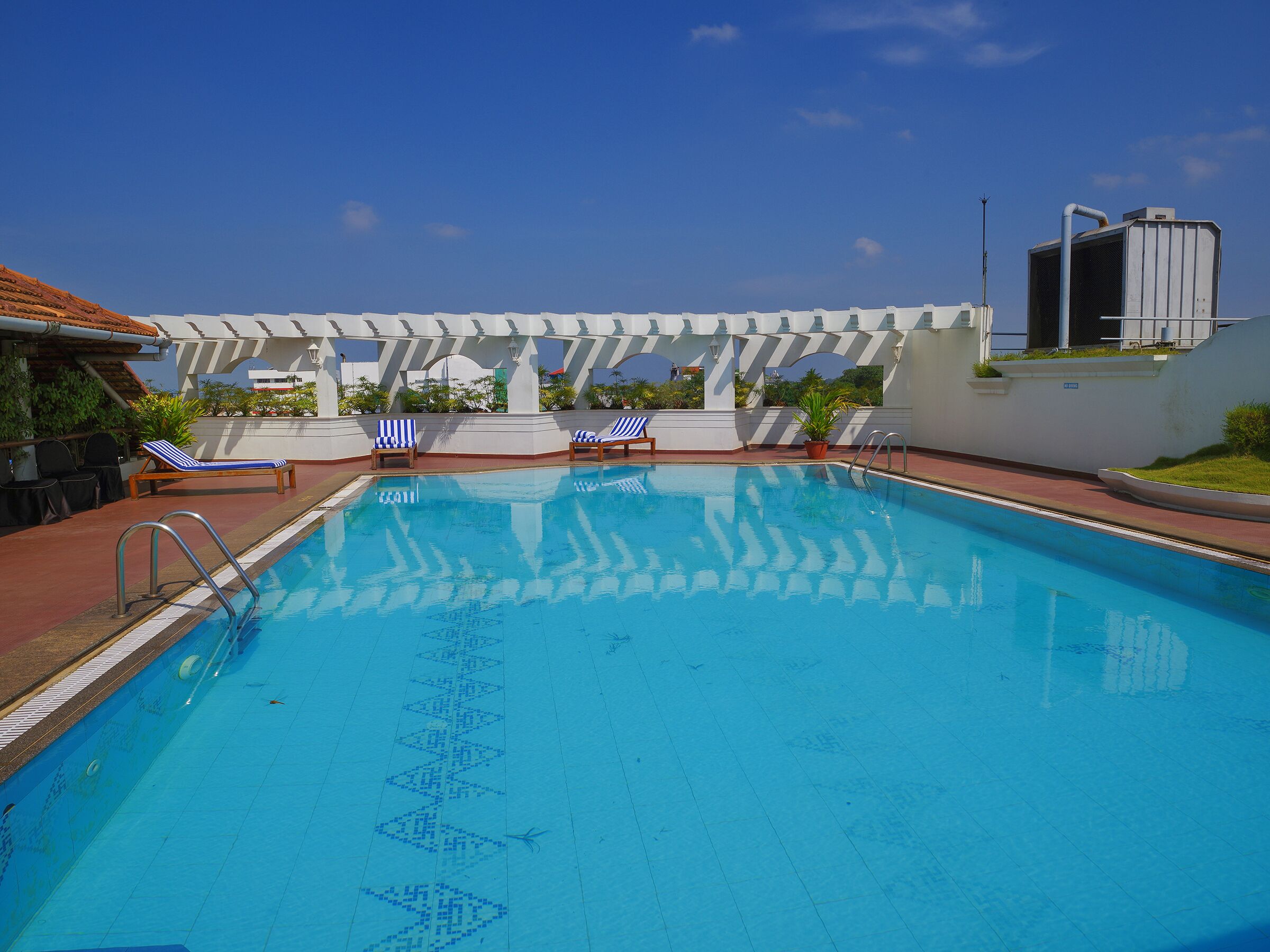 A swimming pool with blue water, surrounded by white columns and blue-striped lounge chairs.