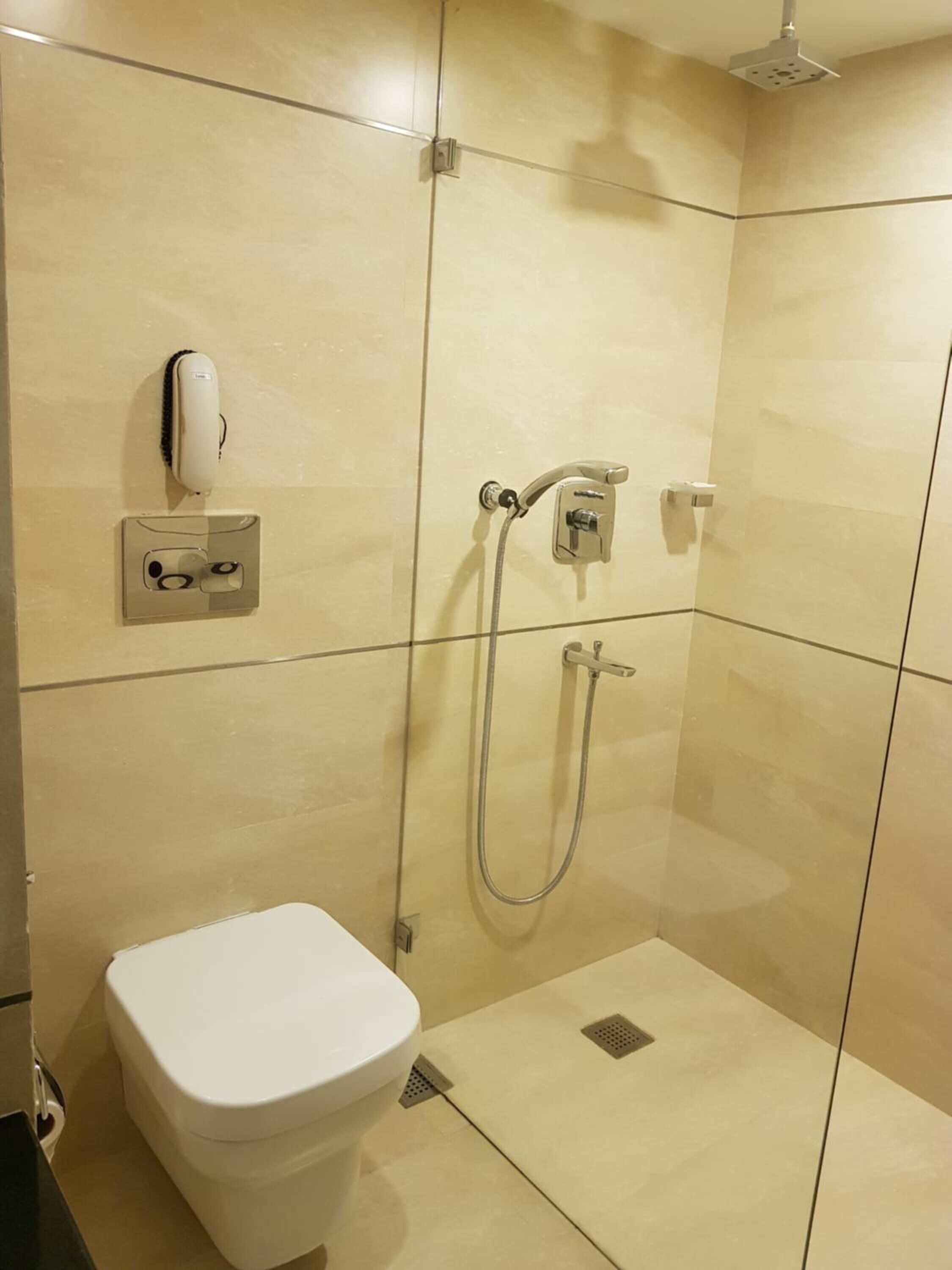 A modern bathroom with a toilet, a handheld showerhead, and a wall-mounted hand dryer.
