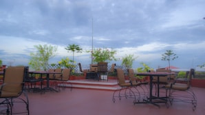 An outdoor patio with tables and chairs, surrounded by a fence and plants. - Hotel Pankaj (Thiruvananthapuram)