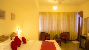 A hotel room with a bed, two armchairs, a desk, and a ceiling fan. - Hotel Pankaj (Thiruvananthapuram)