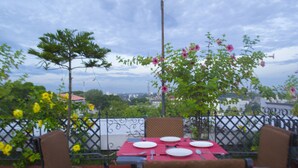 An outdoor dining area with a table set for four, surrounded by chairs, and a view of the cityscape in the background. - Hotel Pankaj (Thiruvananthapuram)