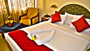 A hotel room with a neatly made bed, a chair, a nightstand, and a lamp. - Hotel Pankaj (Thiruvananthapuram)