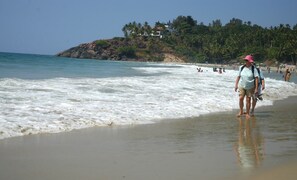 A beach with waves, people, and a hill with buildings and trees. - Hotel Marine Palace (Neyyattinkara)