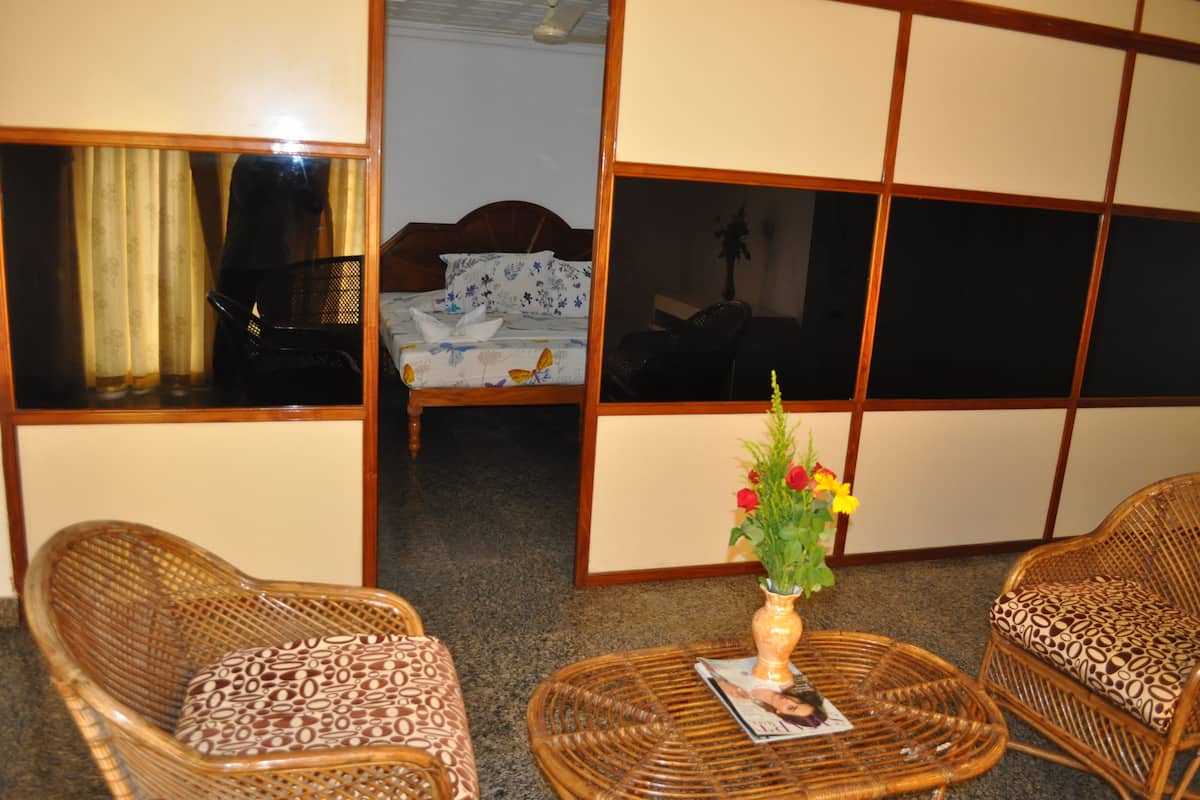 A room with a bed, two wicker chairs, a small table with a magazine, and a vase with flowers.