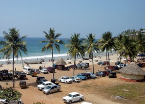 Ein Parkplatz direkt am Strand mit mehreren Autos und Rikschas, Palmen und einer strohgedeckten Hütte.
