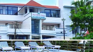 A hotel with a sign indicating A/C and non-A/C rooms, a swimming pool with lounge chairs, and a red-tiled roof. - Hotel Marine Palace (Neyyattinkara)