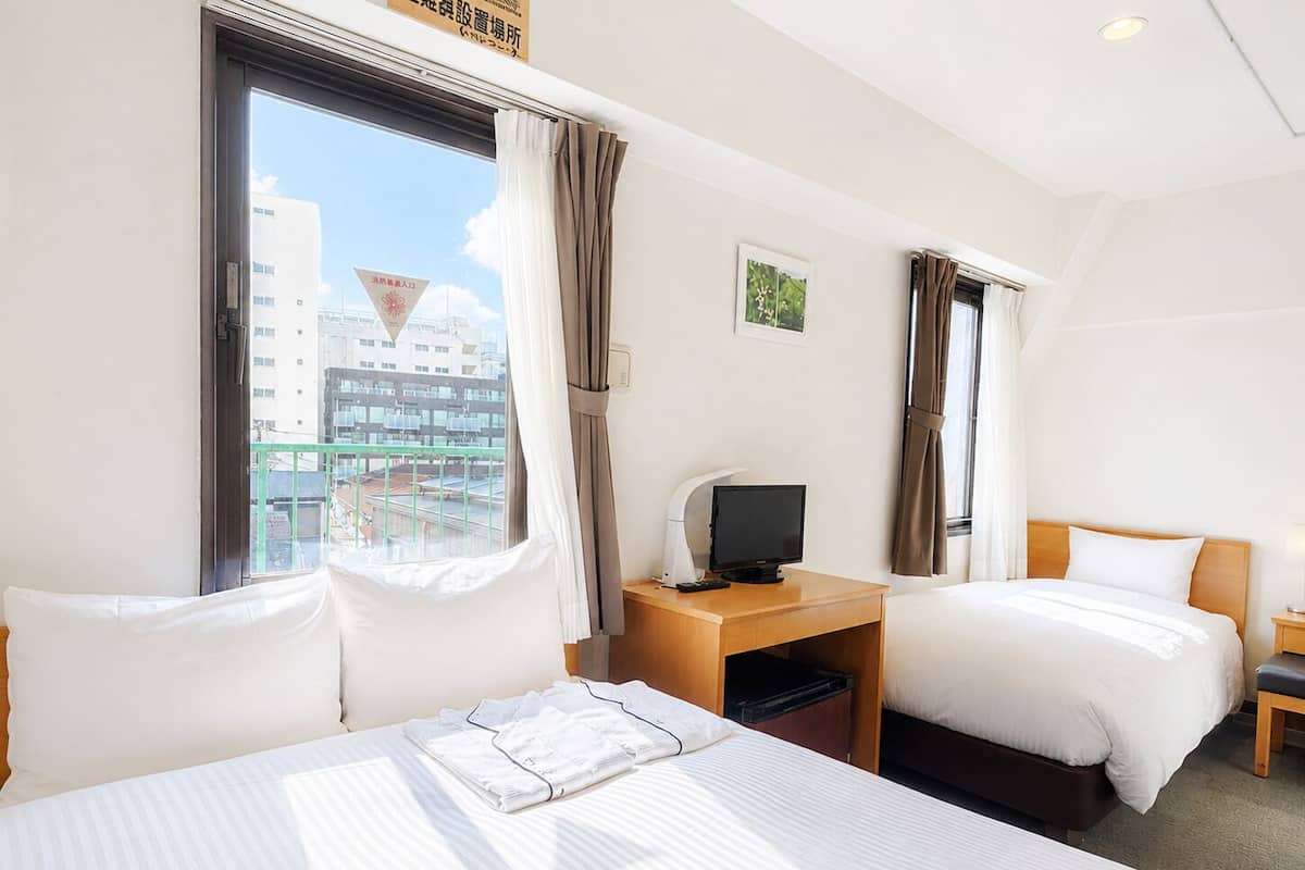 Une chambre d’hôtel avec deux lits, un bureau avec une télévision et une fenêtre donnant sur des immeubles.