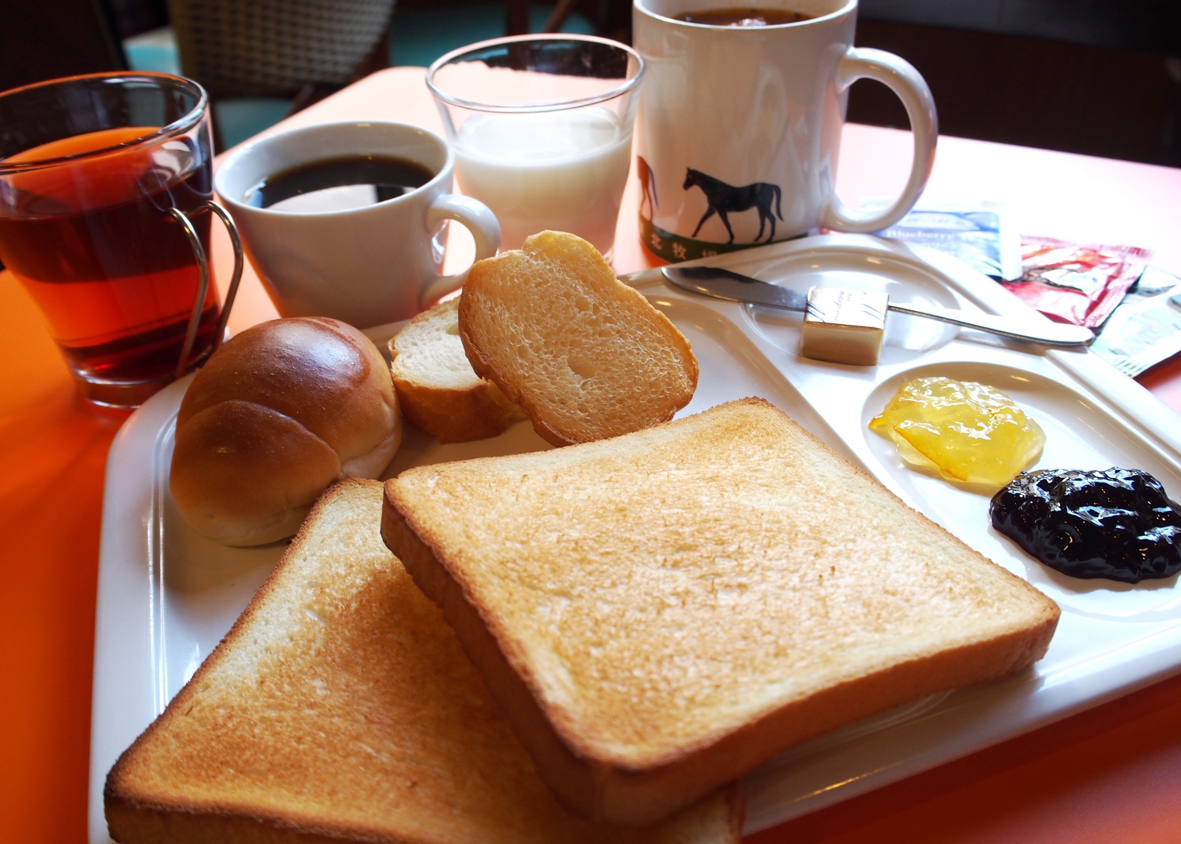 Ett frukostbricka med rostat bröd, smör, sylt, en kopp kaffe, ett glas te och en mugg.