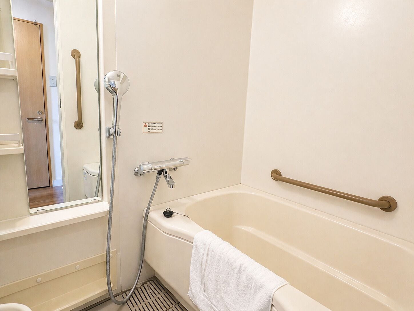A bathroom with a bathtub, a shower, a handrail, and a towel.