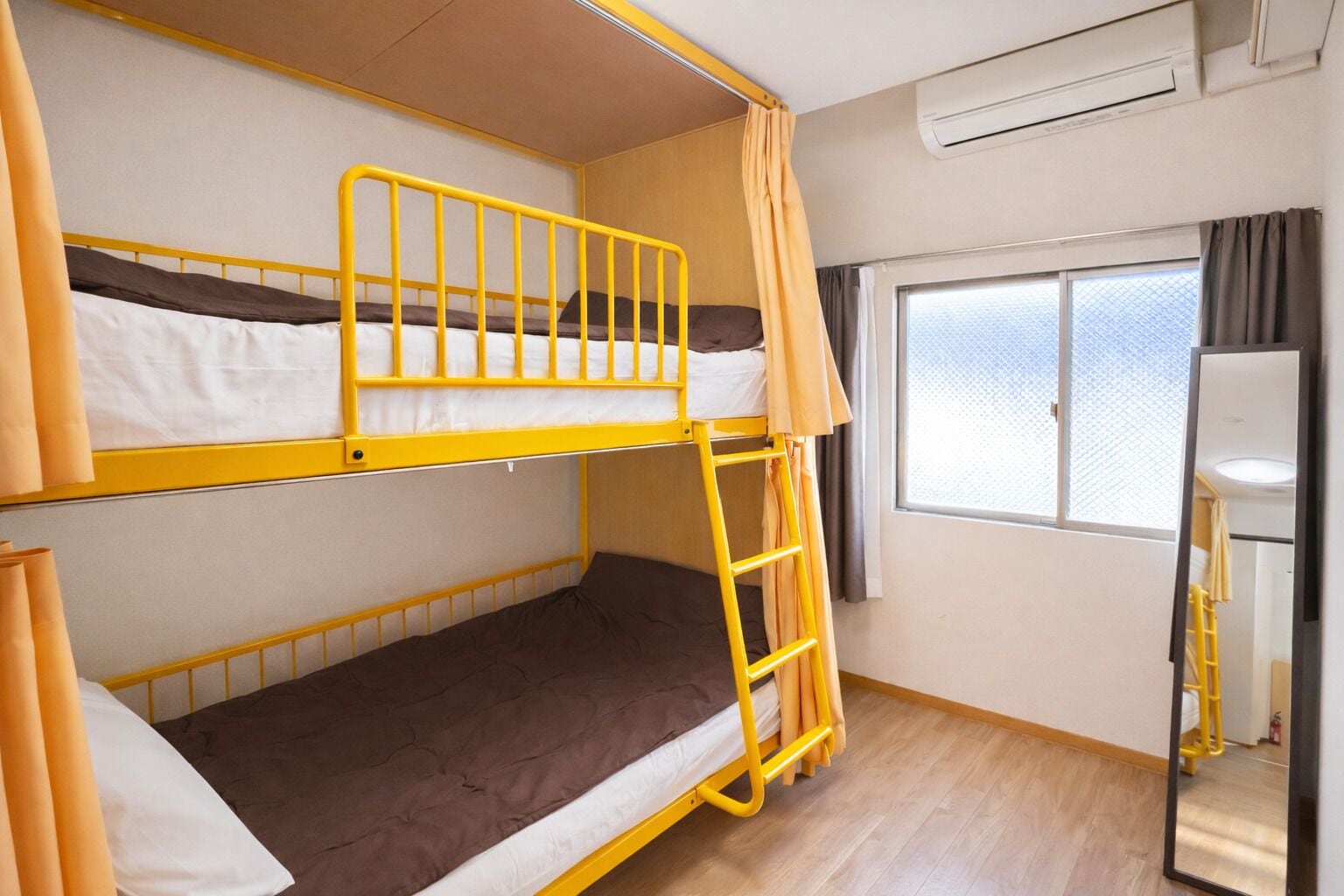 A bunk bed room with a window, an air conditioning unit, and a mirror.