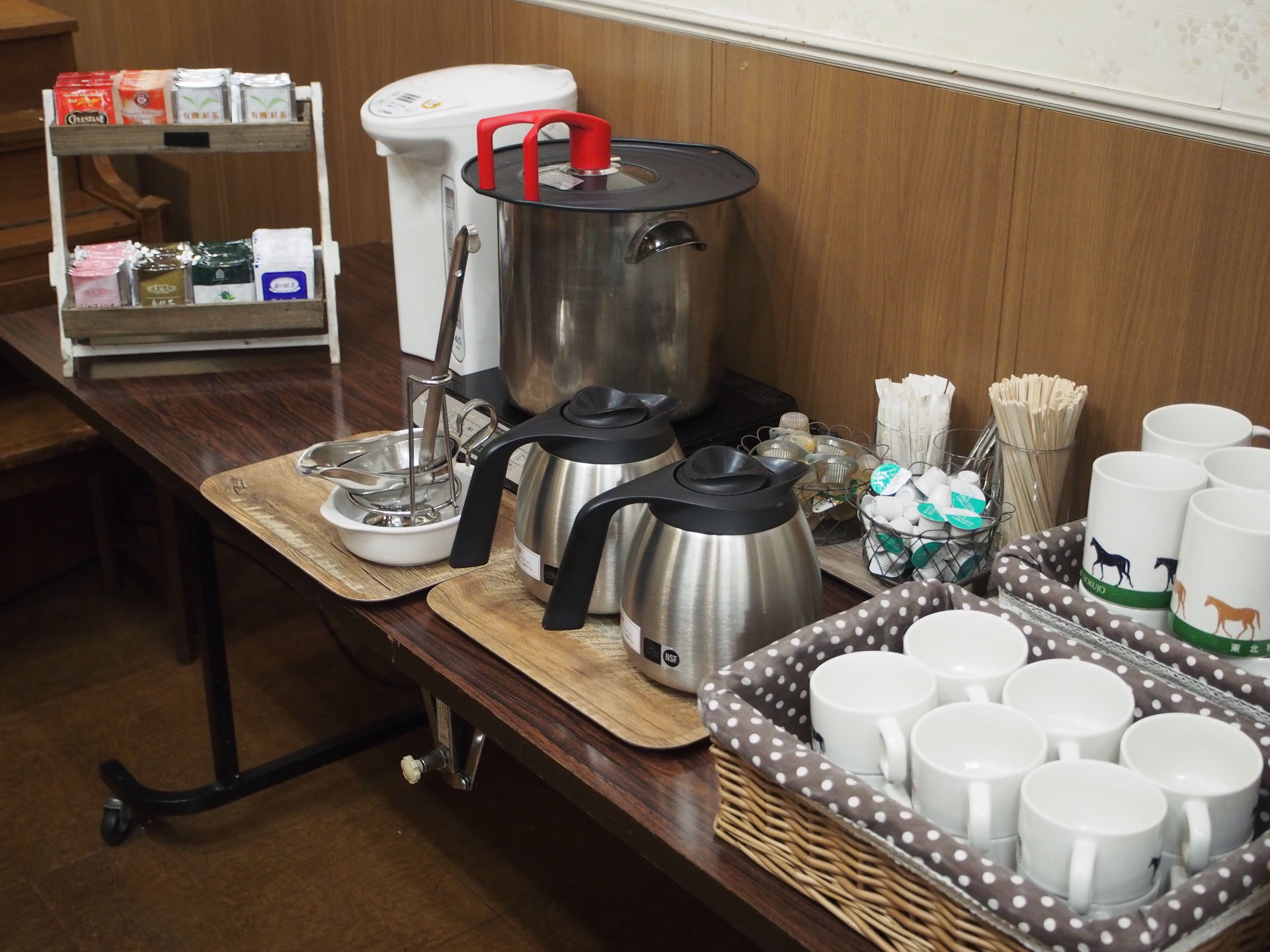 A buffet setup with stainless steel pots, a coffee maker, and a variety of food items on a wooden table.