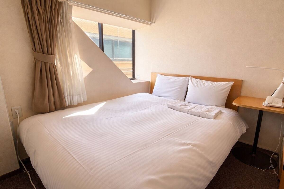 Une chambre d’hôtel avec un grand lit, une table de chevet avec un téléphone et une fenêtre avec des rideaux.