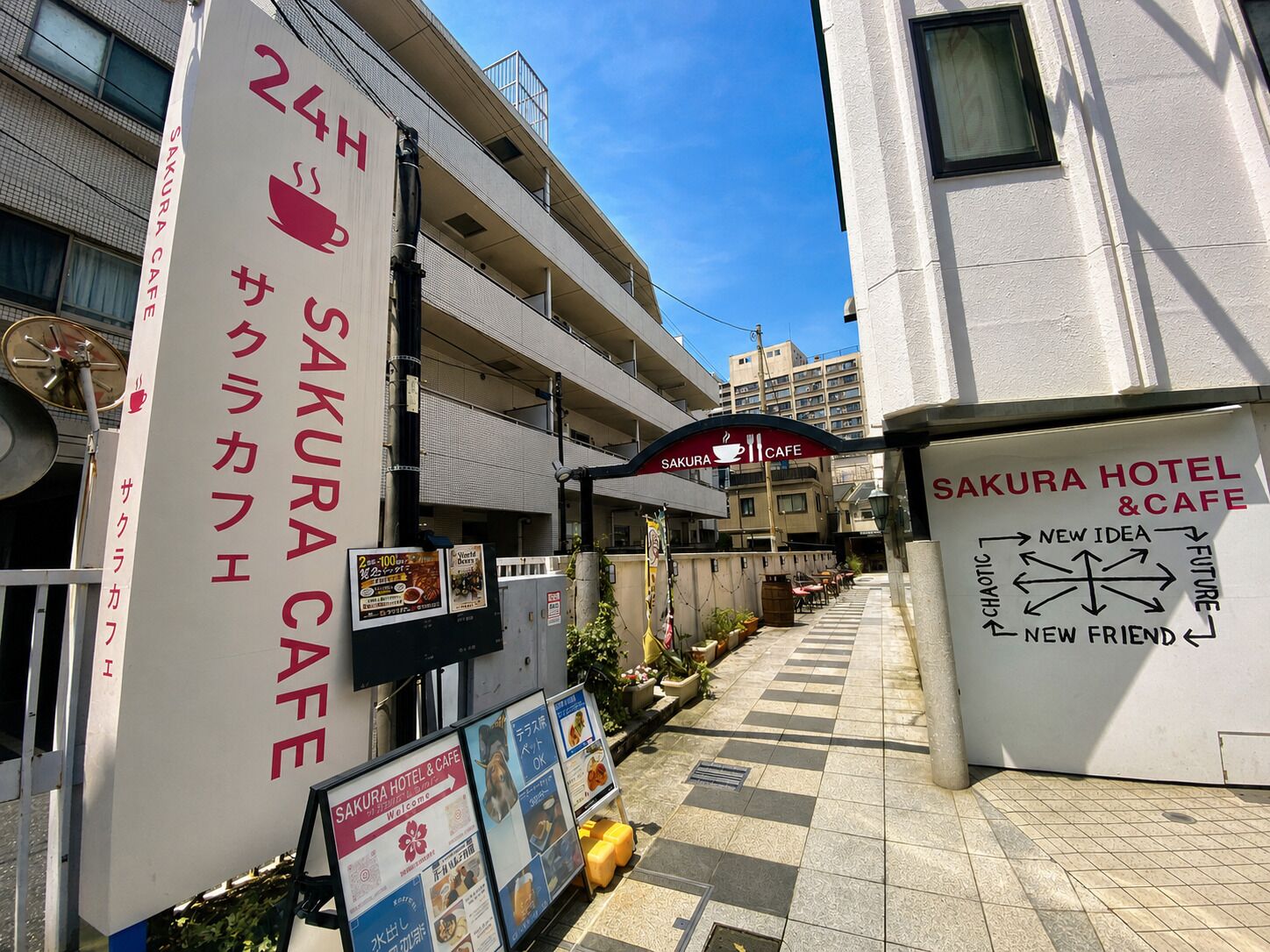 Un hôtel-café Sakura avec un trottoir à carreaux, une enseigne de café et un panneau indicateur pointant vers de nouvelles idées et de nouveaux amis.