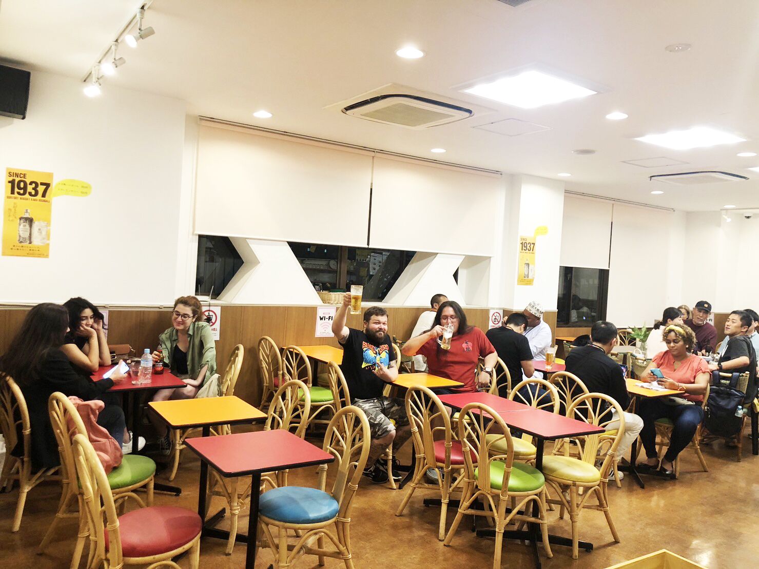 A restaurant with multiple tables and chairs, some with colorful cushions.