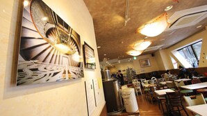 A restaurant interior with tables, chairs, and artwork on the walls. - Sakura Hotel Hatagaya (Tokyo)