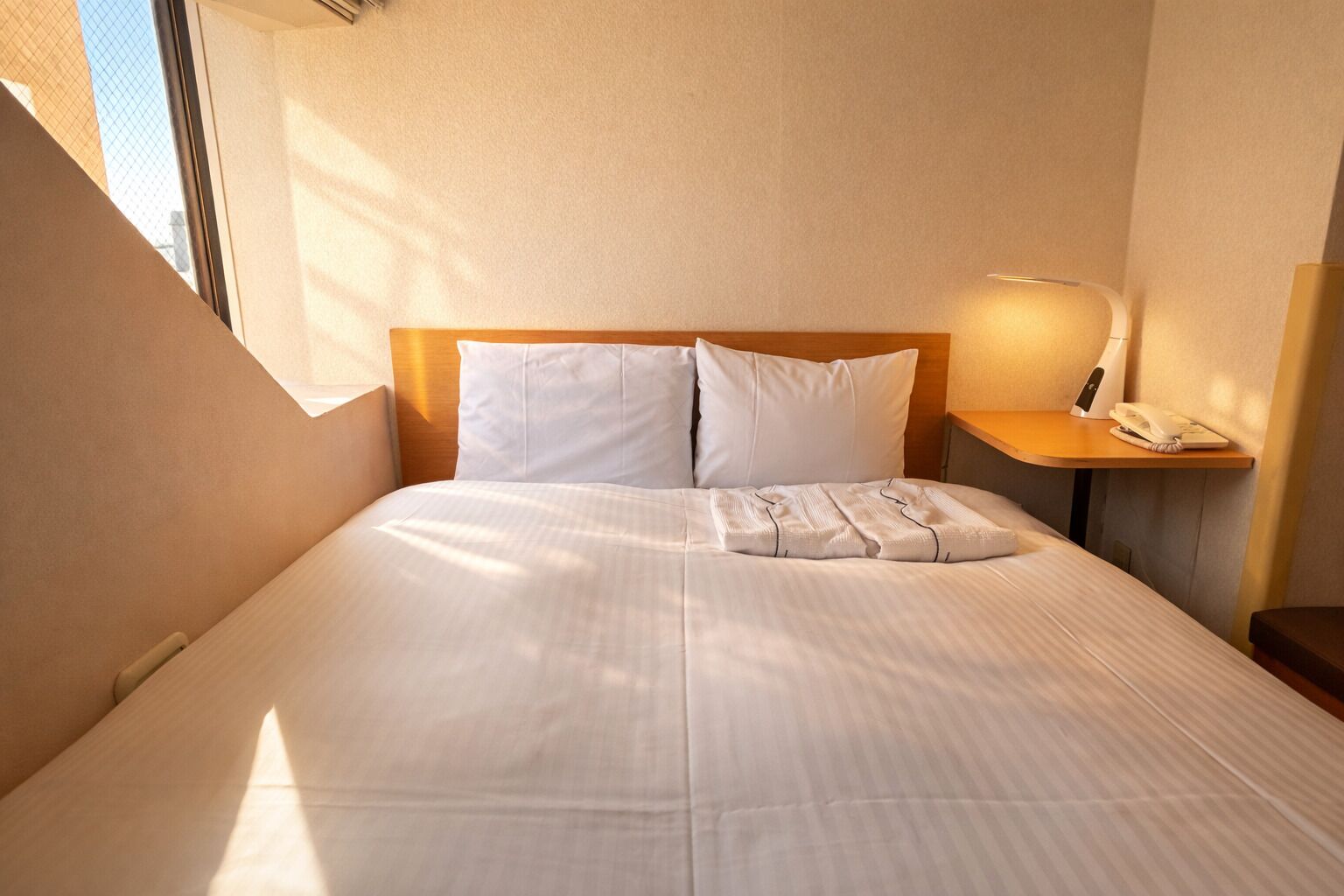 Une chambre d’hôtel avec un lit, des oreillers, une table de chevet avec une lampe et un téléphone.