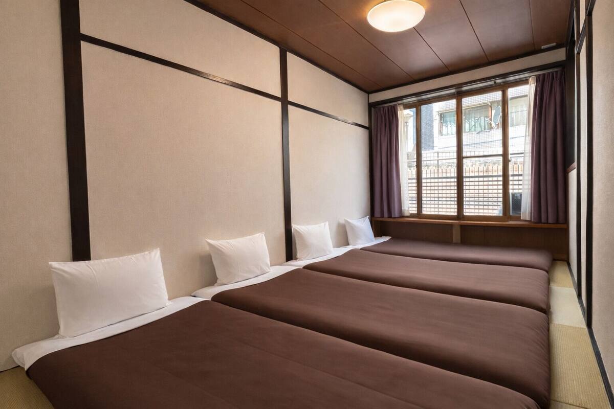 A hotel room with a large bed, a window with curtains, and a view of buildings outside.