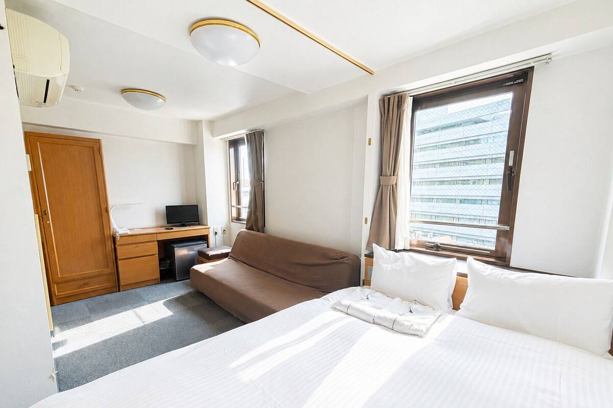 A hotel room with a bed, a desk, a chair, a wardrobe, and a window with curtains.