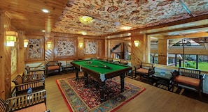 A pool table in a room with wooden walls and ceiling, surrounded by chairs and a patterned rug. - Hotel Heevan Retreat (Baramula)