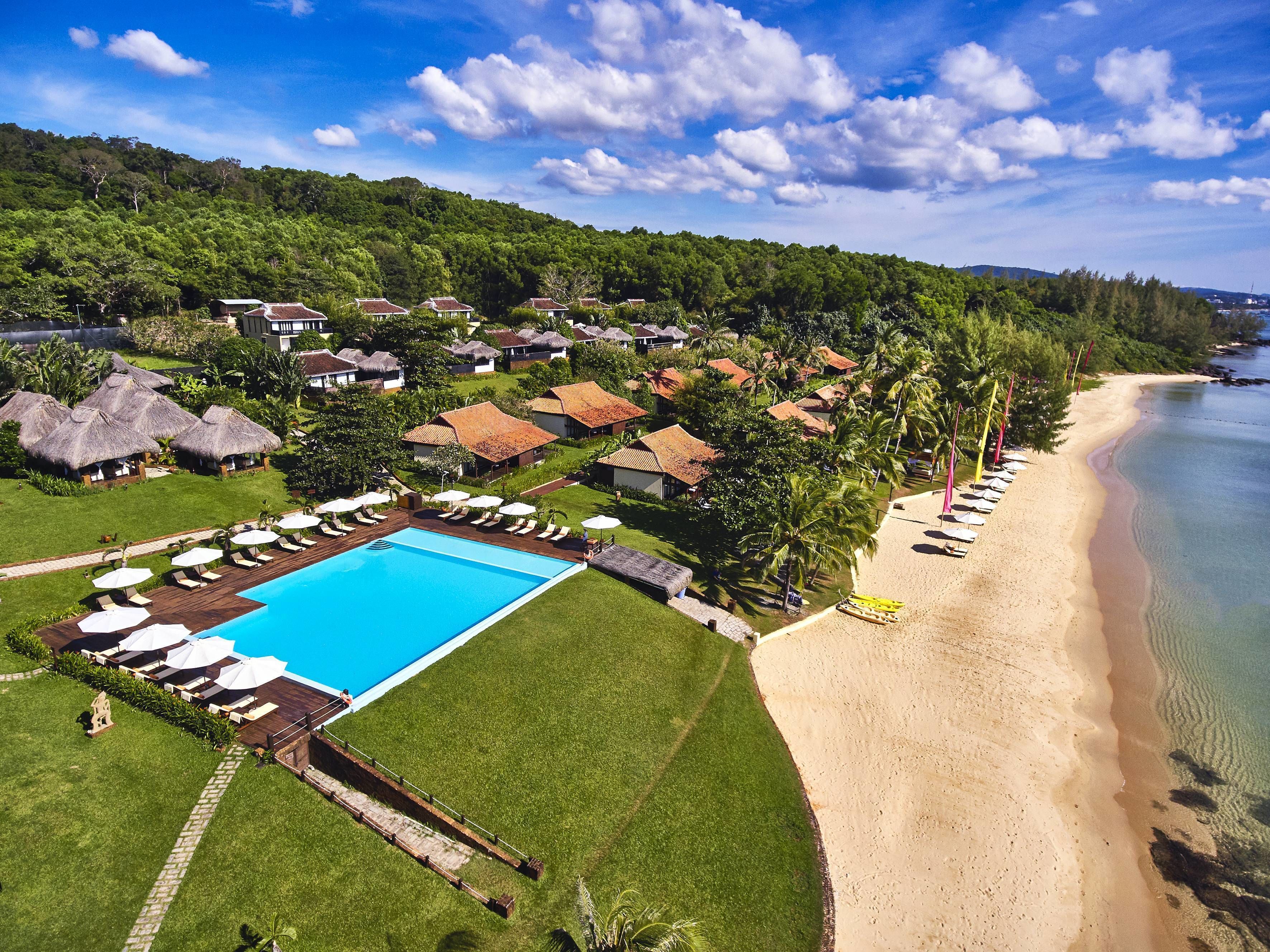 Un resort con piscina, playa y cabañas de techo de paja.