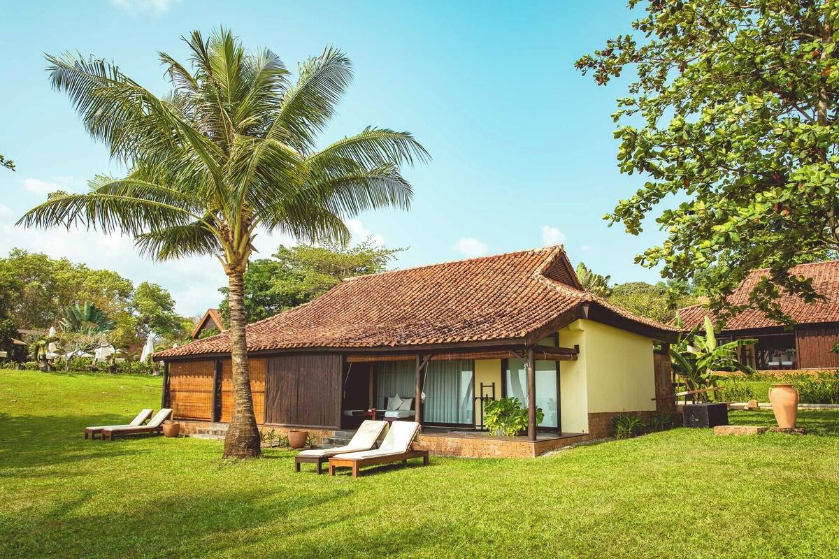 A bungalow with a tiled roof, a covered porch, and a lawn with lounge chairs.