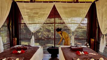 Relax in this serene spa room with two beds, a basin, and a thatched roof.