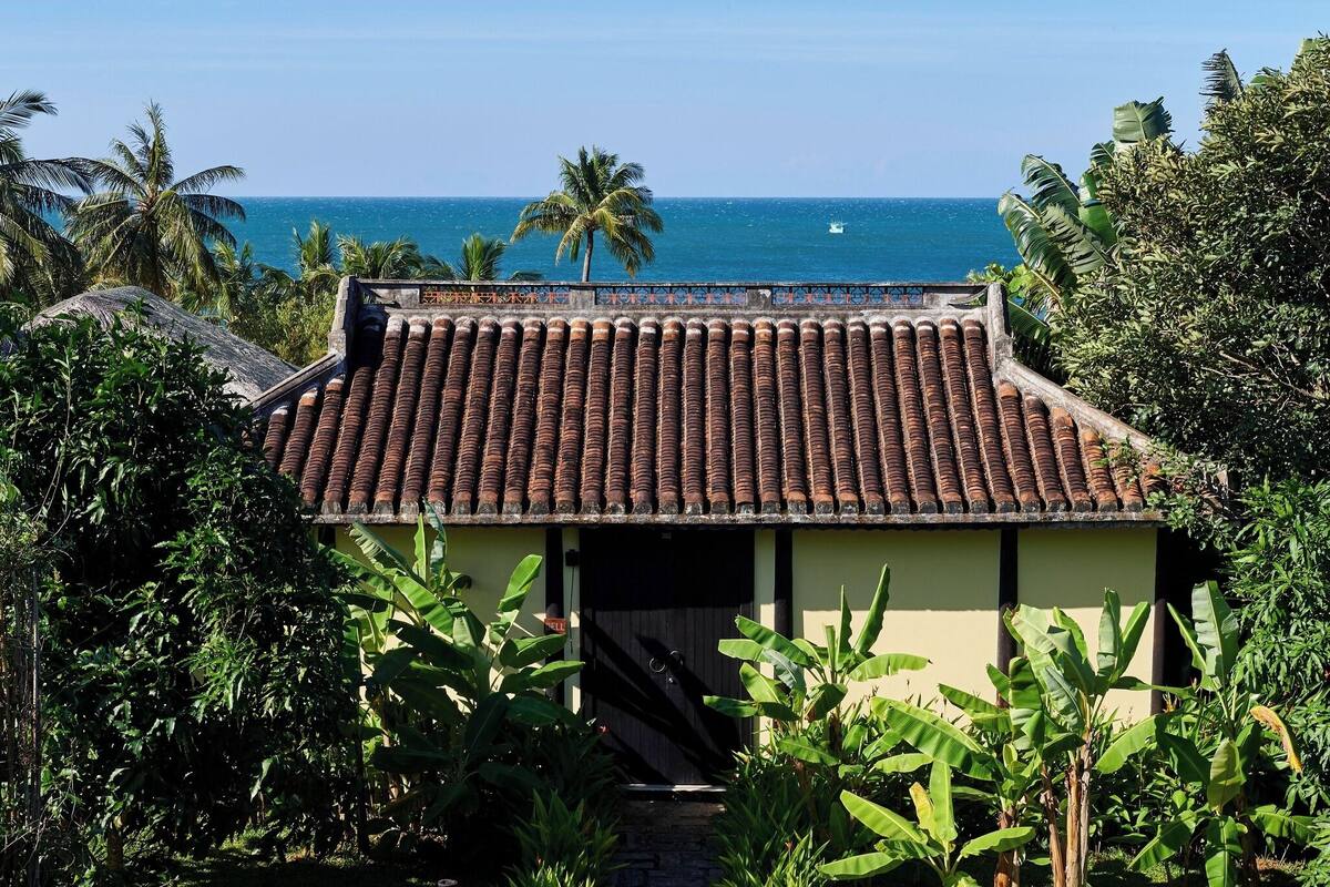 A building with a tiled roof, surrounded by lush greenery and overlooking a clear blue sea.