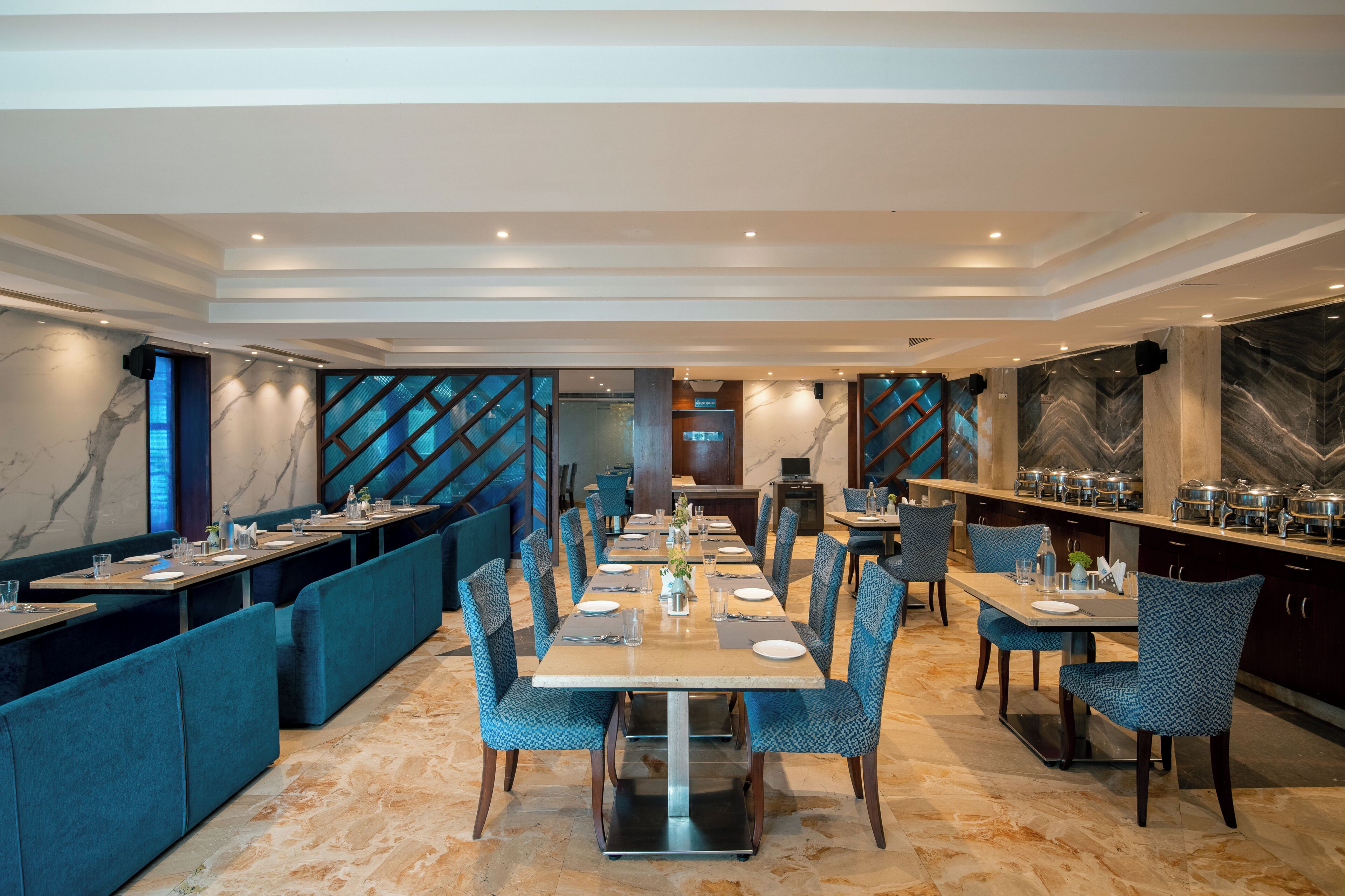A modern dining area with a long table, blue upholstered booths, and marble walls.
