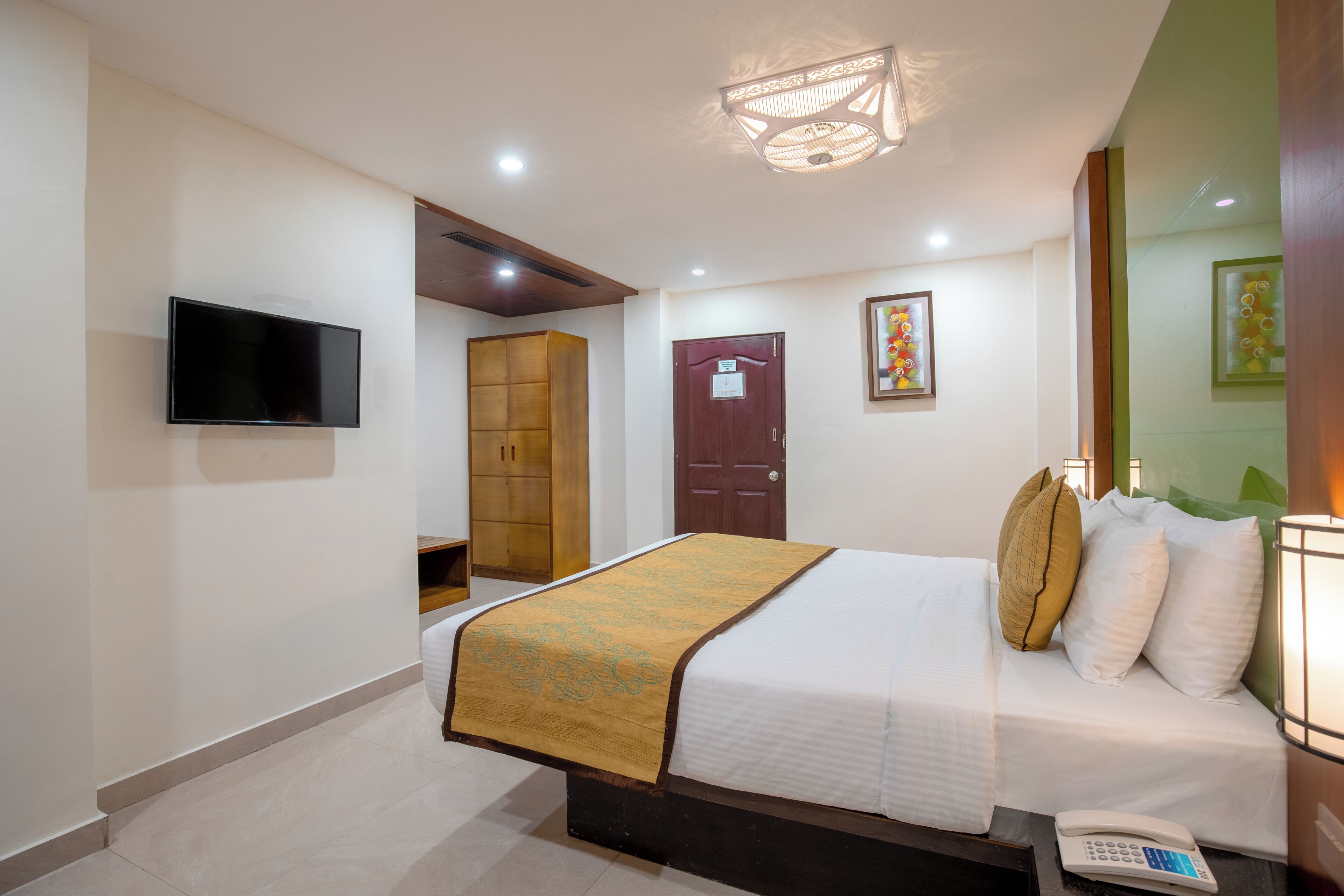 A hotel room with a bed, a telephone, a television, a wardrobe, and a door.