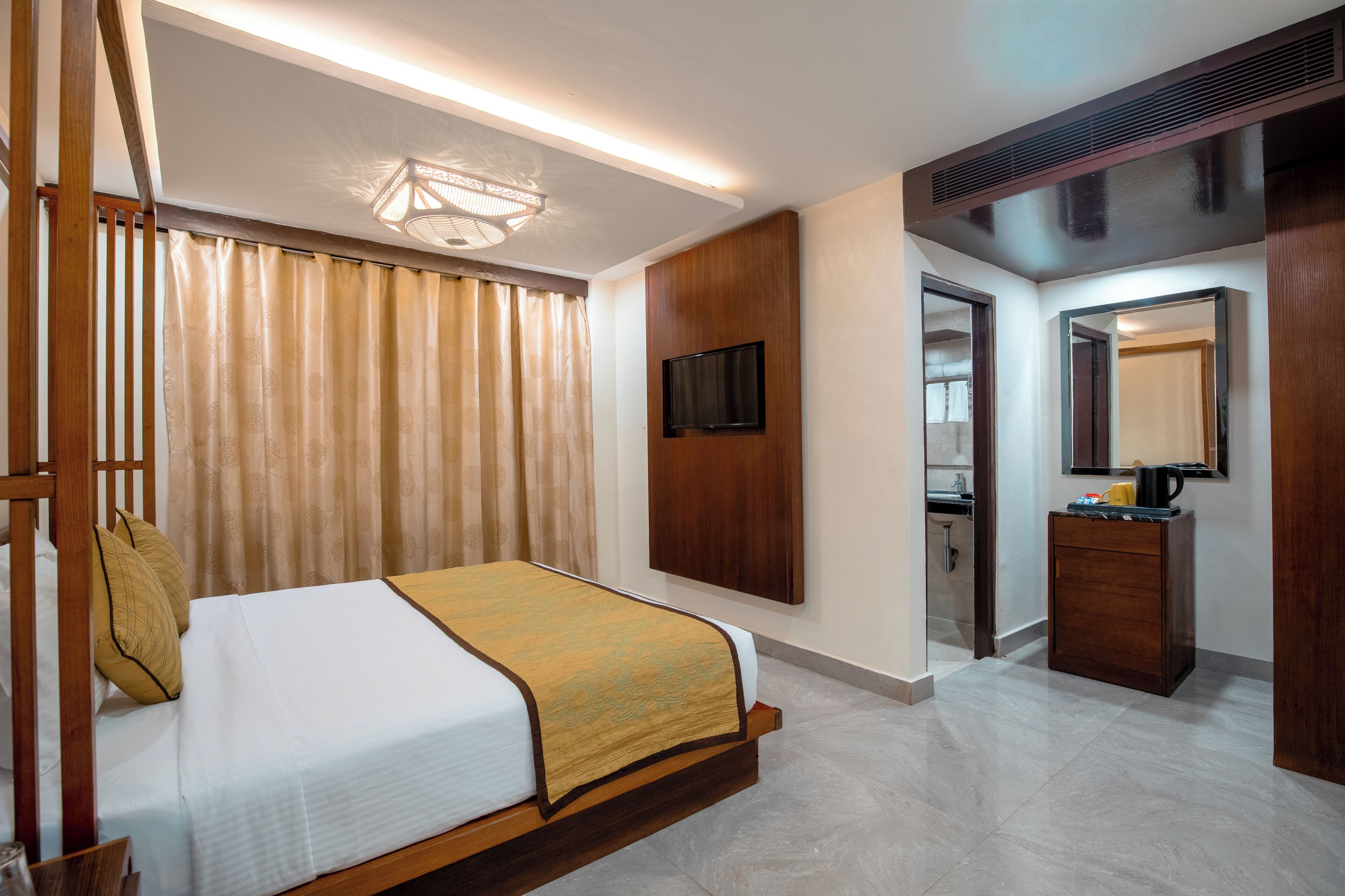 Habitación de hotel con cama, televisor, espejo, una pequeña alacena y puerta que da a un baño.