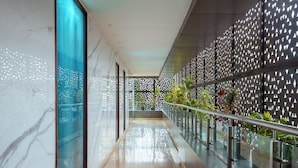 A modern corridor with reflective floors, glass railings, and a patterned wall with greenery. - TSG EMERALD VIEW HOTEL AND SPA (Port Blair)