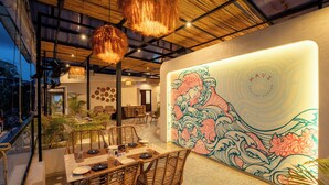 A restaurant with a dining area featuring a large mural, wicker furniture, and hanging light fixtures. - TSG EMERALD VIEW HOTEL AND SPA (Port Blair)