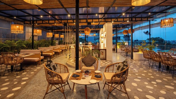 A restaurant with wicker furniture, a central table, and hanging lamps. - TSG EMERALD VIEW HOTEL AND SPA (Port Blair)