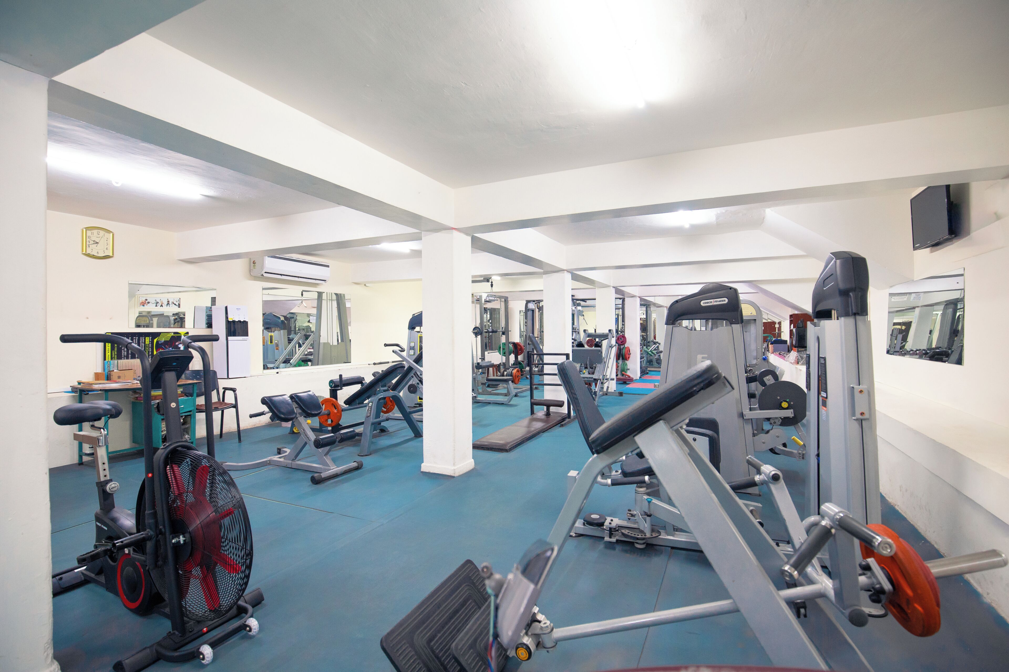 A gym with various exercise equipment, a clock on the wall, and an air conditioning unit.