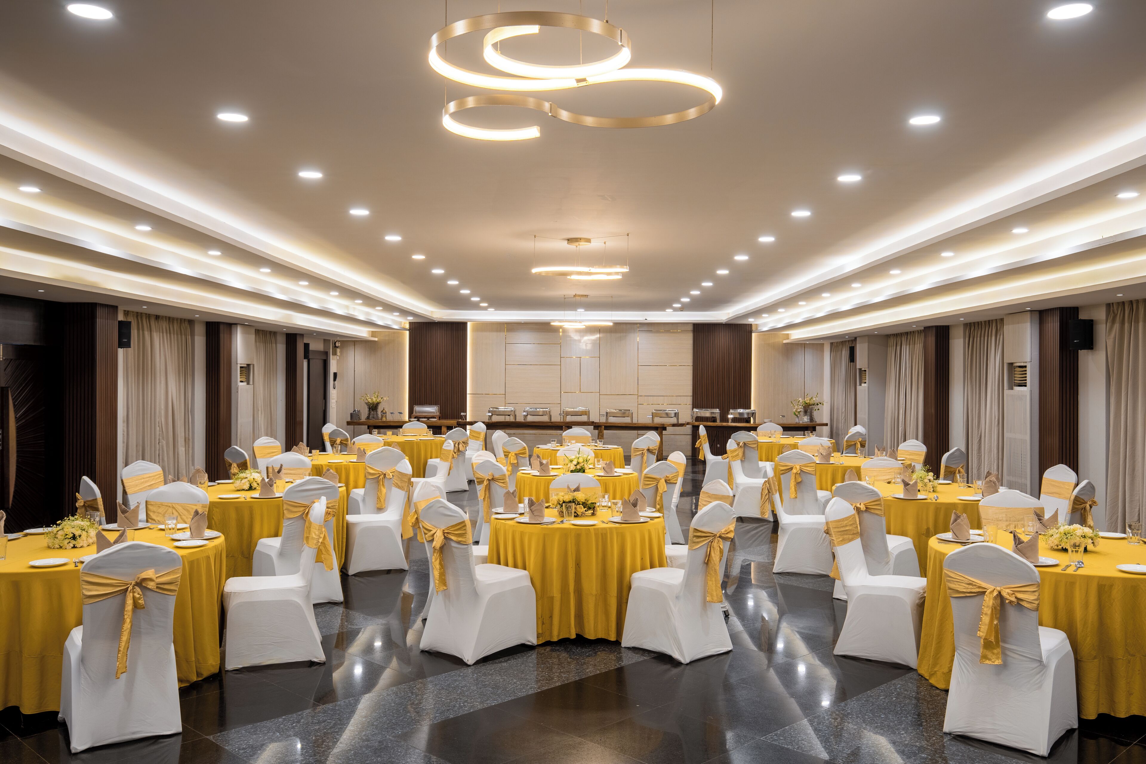 A banquet hall with round tables, white chairs, and yellow tablecloths.