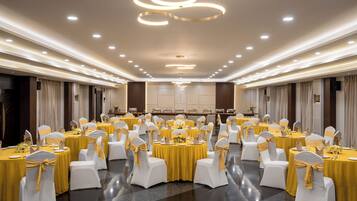 A banquet hall with round tables, white chairs, and yellow tablecloths.