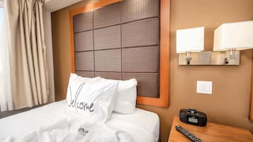 A hotel room with a large bed, a bedside table with a remote control, and a wall-mounted lamp.
