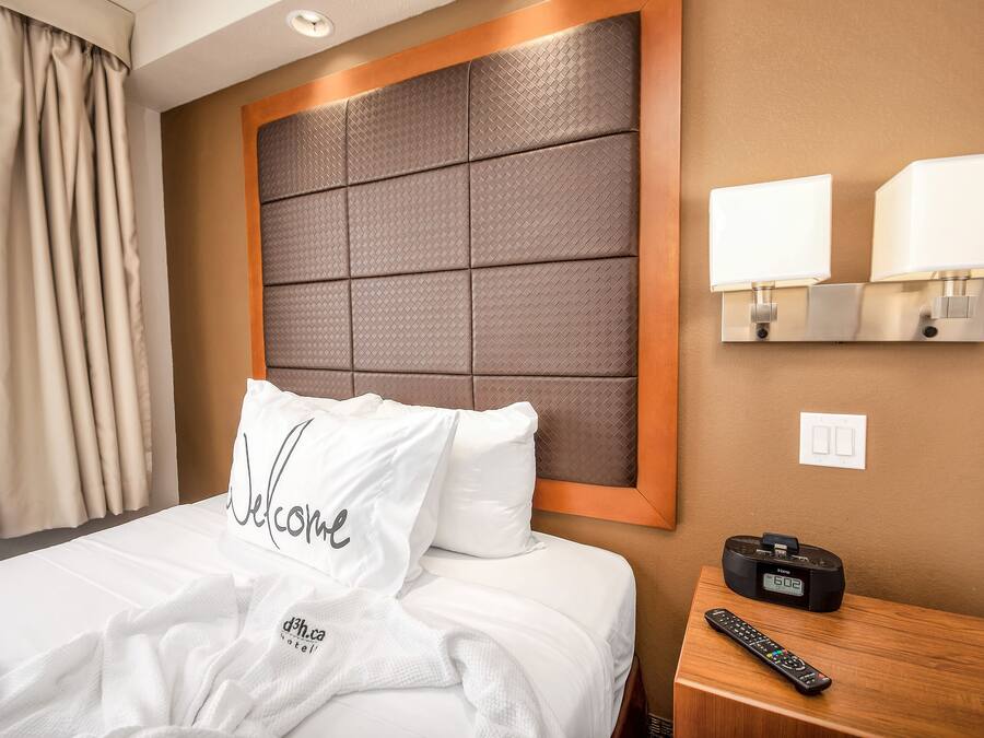 A hotel room with a large bed, a bedside table with a remote control, and a wall-mounted lamp.