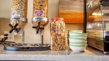 Una encimera de cocina con dos dispensadores de cereal Kellogg's, un tarro de cereales variados y una pila de tazones verde y blanco.